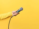 Hand mit Mikrofon vor gelbem Hintergrund