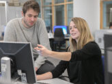 Zwei Studierende die gemeinsam in einen Computer blicken.