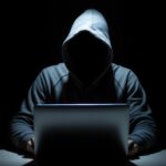 Person in Kapuzenpulli vor Laptop. Die Kapuze verdeckt das Gesicht. In Grau-/Schwarztönen gehalten. Illustration für einen "Incel".